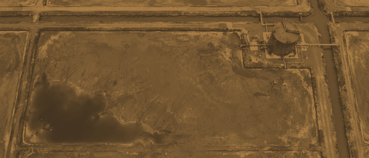 A drained crystalliser from 300 metres holding a shallow film of leftover liquor in its low corner, a drain channel running to a squat storage tank on the bank.